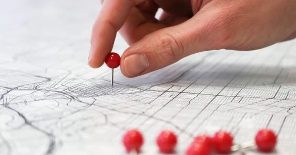 A hand placing a red pin on a city street map, with more pins lined up nearby