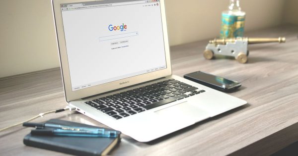 A laptop open to the Google search page on a desk beside a phone and a notebook
